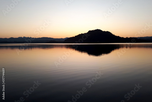 The silhouette of the mountain reflected on the evening water. © Lapassawat