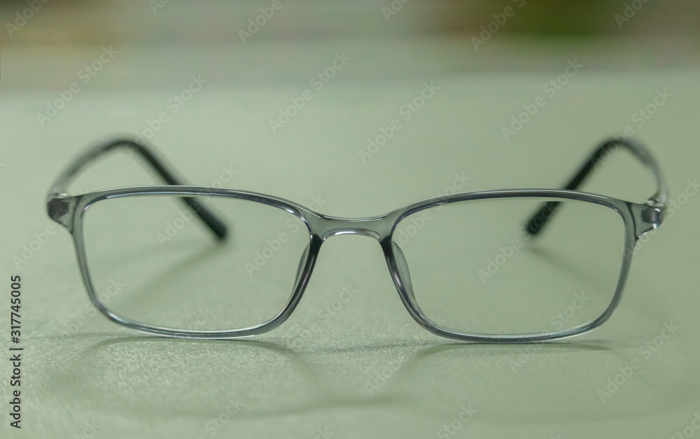 clear plastic glasses, eyes closed, shot close-up, on a blurred green background. Concept: beautiful eyes, beautiful smile, vision, look both with clear clear plastic glasses, eyes closed, shot close-up, on a blurred green background. Concept: beautiful eyes, beautiful smile, vision, look both with clear