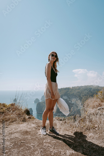Travel girl in swimsuit is standing in front of beautiful coastline view from Saren Cliff Point, Nusa Penida, Indonesia