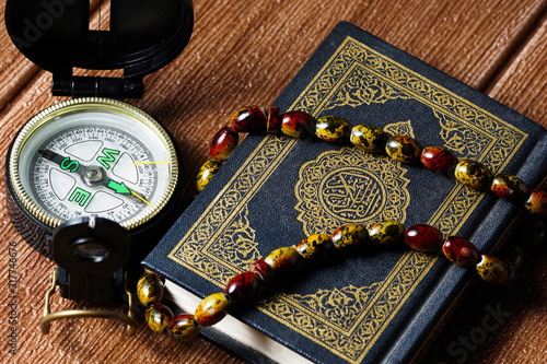 The Quran with rosary beads or “tasbih” and compass on wooden surface. Arabic characters means : Holy Quran, the Holy book of Islam. Islamic concept. photo