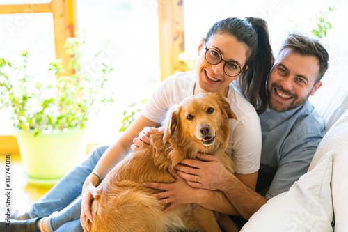 Happy couple with a golden retriever dog sitting on a sofa smiling and positive photo
