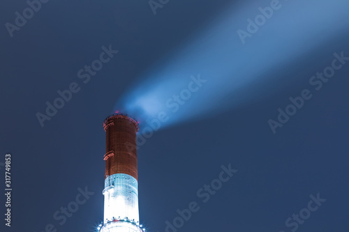 The illuminated red and white tube or pipe of the thermal power plant on the background of blue night or evening sky with the vapour or smoke emition photo