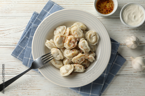 Plate of dumplings with spices on white wooden background, top view