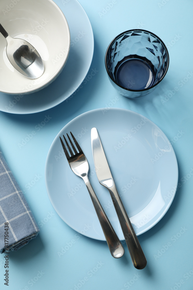 Tableware and cutlery on blue background, top view