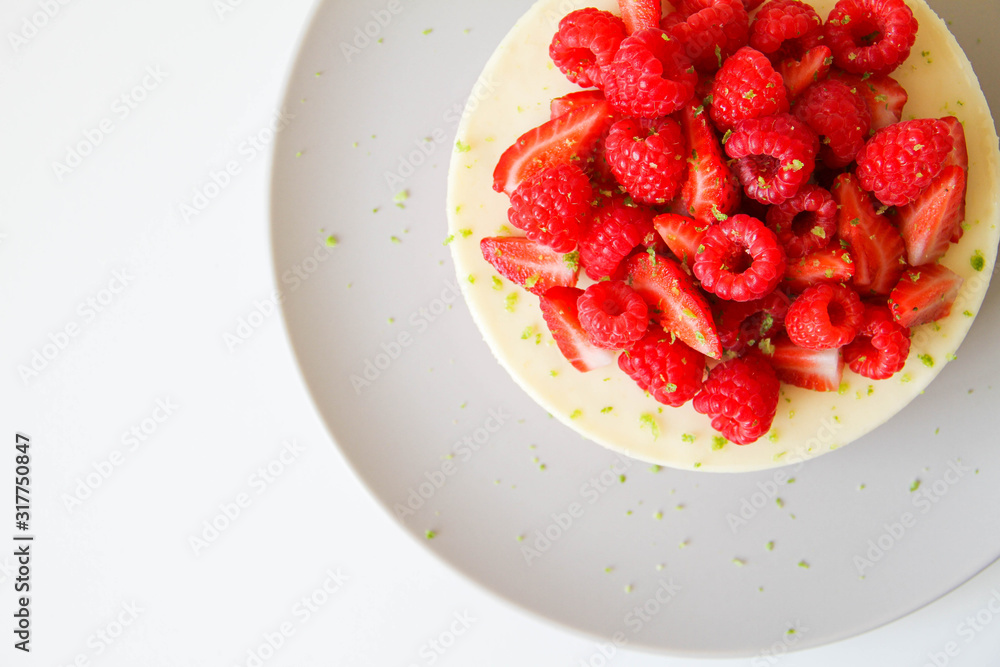 French dessert. Lime mousse cake with lime biscuit and red berries filling. Cake decorated with fresh berries and a lime zest. Cake is on a light grey plate, on a light background. French dessert. Lime mousse cake with lime biscuit and red berries filling. Cake decorated with fresh berries and a lime zest. Cake is on a light grey plate, on a light background.