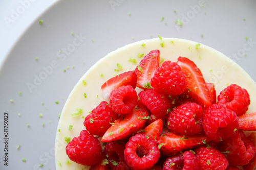 French dessert. Lime mousse cake with lime biscuit and red berries filling. Cake decorated with fresh berries and a lime zest. Cake is on a light grey plate  on a light background. 