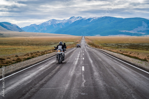 A motorcyclist with his hand raised in greeting, riding along the Chuysky highway at dawn, landscape with a highway. Russia, mountain Altai