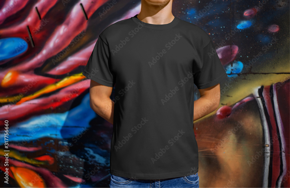 Mockup black male t-shirt on a young guy against the background of a wall with graffiti, front view.