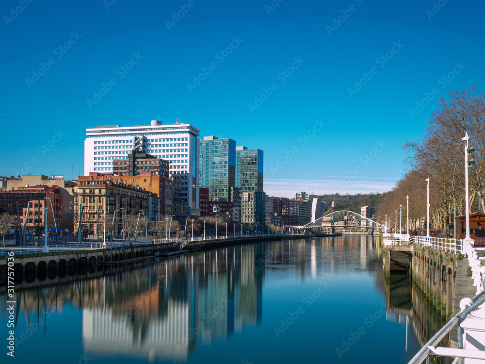 Buildings reflected in the estuary of Bilbao on a blue sky day