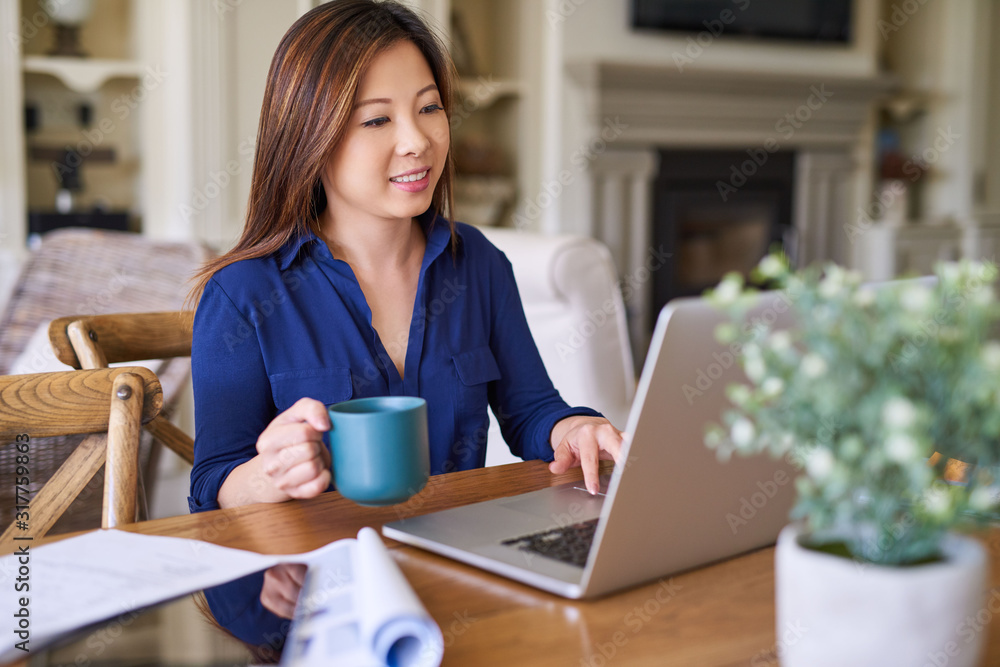 Smiling young Asian businesswoman drinking coffee while working at home Smiling young Asian businesswoman drinking coffee while working at home