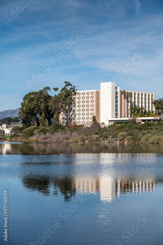 Goleta, CA, USA - January 2, 2020: UCSB, University California Santa Barbara. Blue Campus lagoon separated from blue ocean and sky by green-yellow dunes. Oil drill platform on horizon. © Klodien