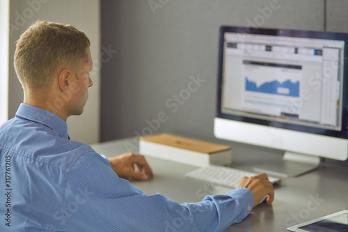 Young businessman working in office, sitting at desk, looking at laptop computer screen, smiling