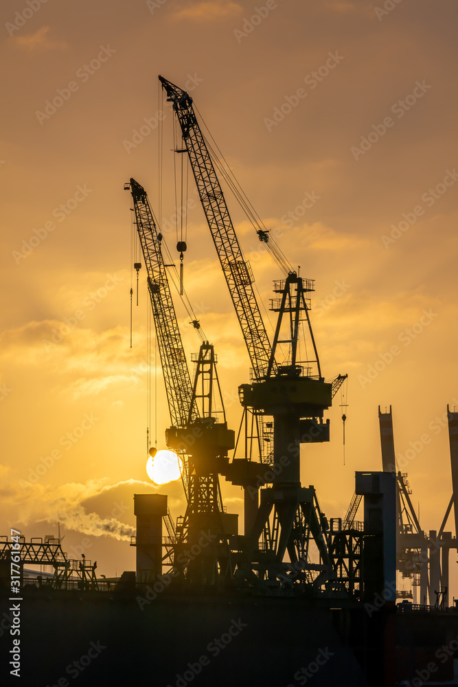 Hamburg, Germany. Cranes silhouetted against the evening sky in the harbor at dusk. The Port of Hamburg (German: Hamburger Hafen) is a sea port on the river Elbe. It is Germany's largest harbor.