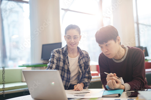 Two students sitting at the table and using laptop computer in their study in the classroom