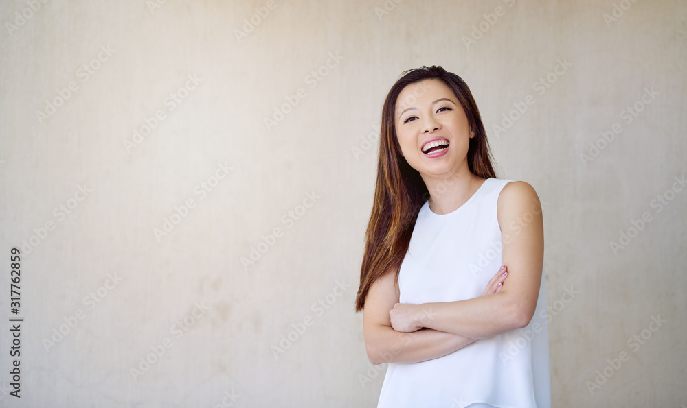 Laughing young Asian woman standing by a wall outside Laughing young Asian woman standing by a wall outside