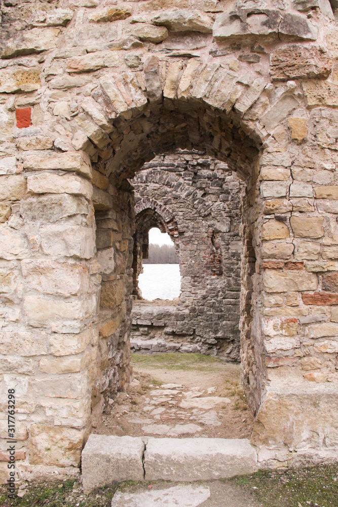 Portal in the medieval castle wall. The wall built of rocks and bricks with a window in the middle. 