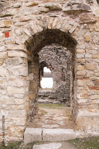 Portal in the medieval castle wall. The wall built of rocks and bricks with a window in the middle. 