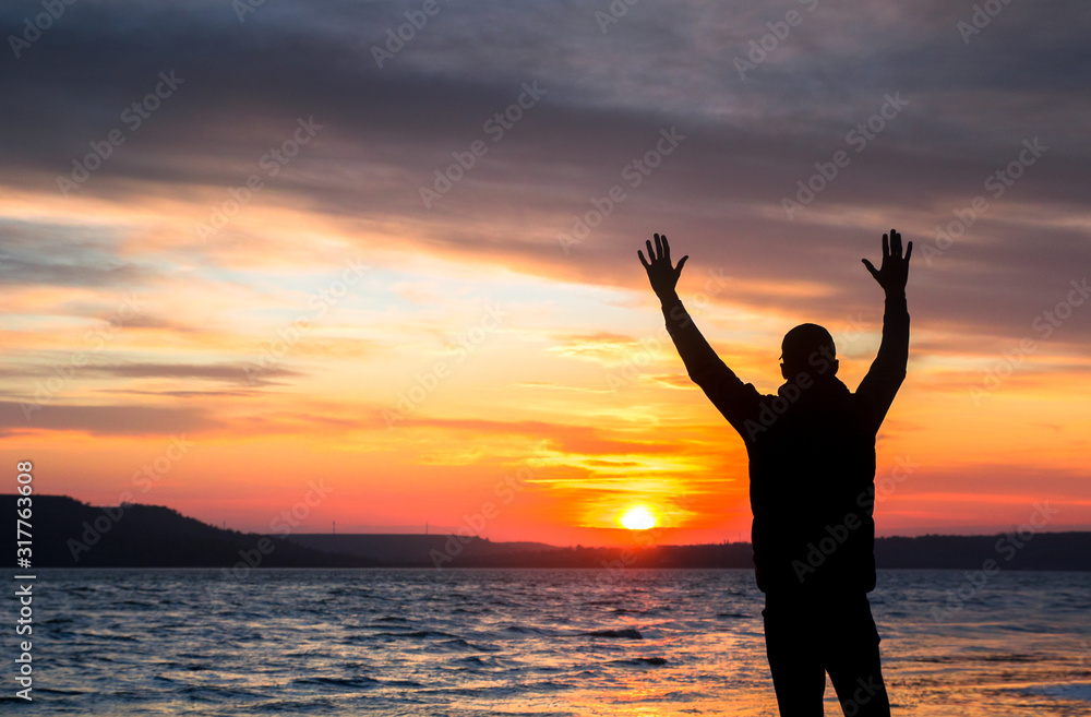 silhouette of a happy unrecognizable man at sunset on the lake