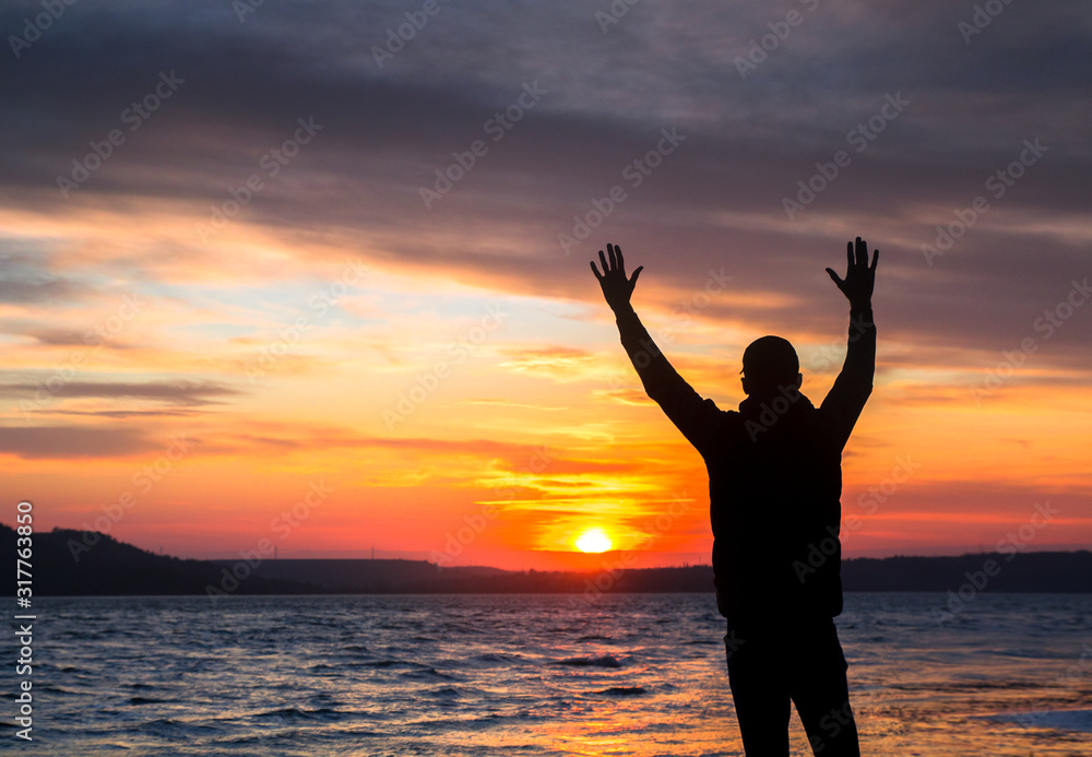 silhouette of a unrecognizable happy man at sunset on the lake