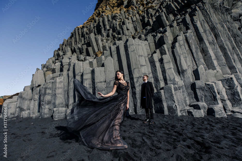 Young beautiful couple bride and groom in black clothes walks near basalt stones in Iceland Young beautiful couple bride and groom in black clothes walks near basalt stones in Iceland