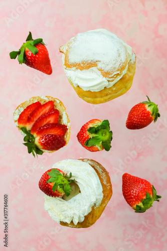 Fototapeta Naklejka Na Ścianę i Meble -  Funny flying buns Laskiaispulla in motion falling on pink concrete background. Wheat bun with top cut off and filled with a mix of milk and almond paste (or strawberry jam), topped with whipped cream.