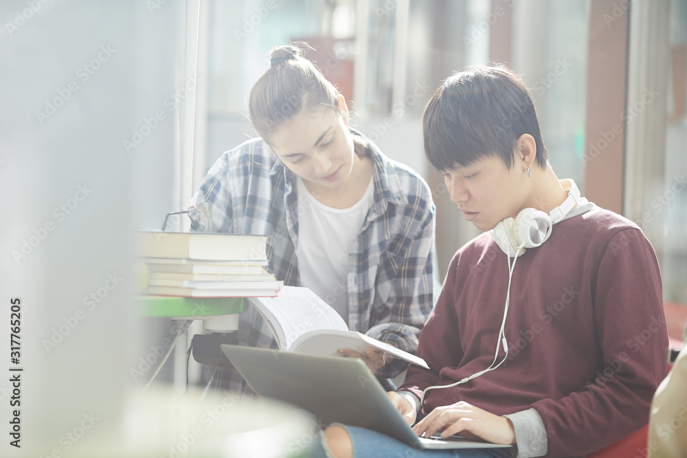 Two college students using laptop computer and reading books they preparing for exams together Two college students using laptop computer and reading books they preparing for exams together