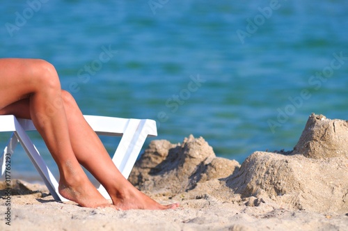 Legs of woman on sunbed near still sea water edge