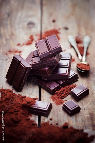 Bittersweet chocolate, tea spoons and cocoa powder on wood