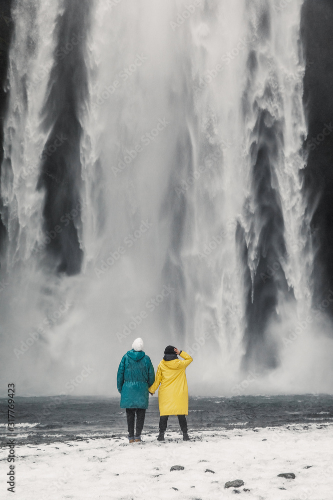 young beautiful couple travelers girl in yellow clothes a man in green clothes stands near a waterfall in Iceland young beautiful couple travelers girl in yellow clothes a man in green clothes stands near a waterfall in Iceland