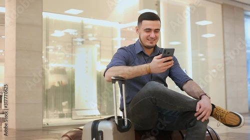 Young men on business trip uses mobile Internet at the airport. Laughs and writes a message in love