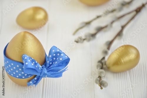 gold easter eggs with decorative blue bow with willow branches on a light background with space for text