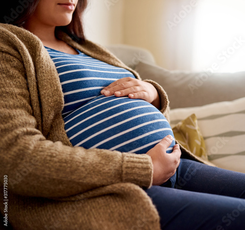 Young pregnant woman affectionately holding her tummy at home