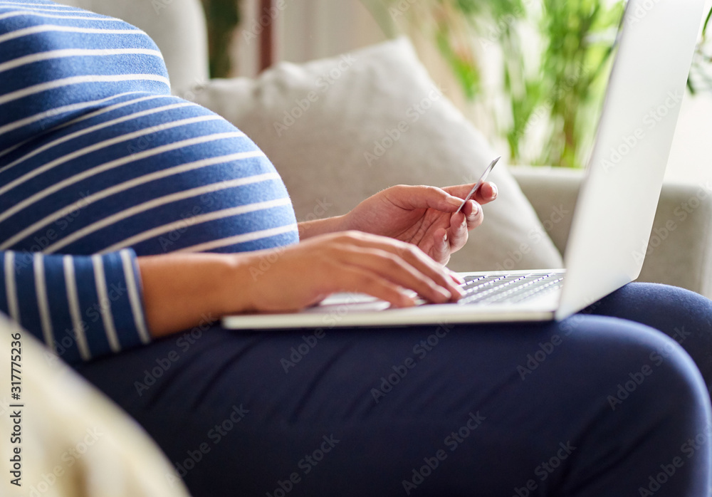 Young pregnant woman sitting on her sofa shopping online Young pregnant woman sitting on her sofa shopping online