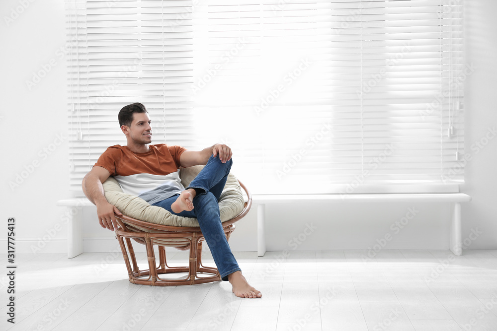 Attractive man relaxing in papasan chair near window at home. Space for text
