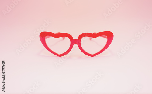Red glasses in the shape of hearts on a pink background.