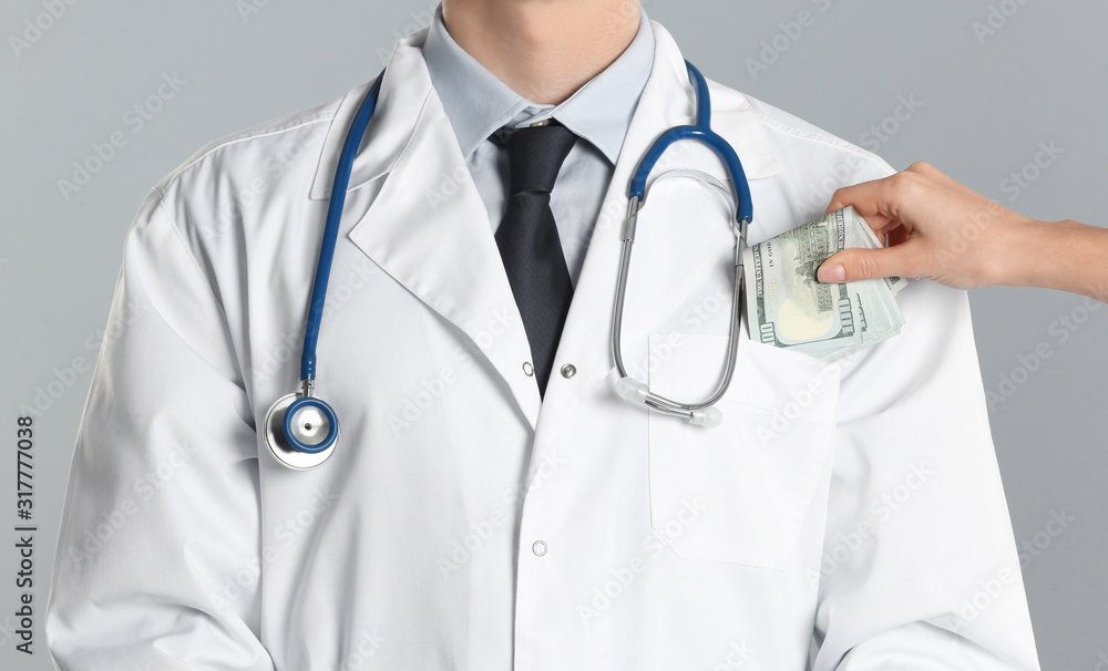 Patient putting bribe into doctor's pocket on grey background, closeup. Corruption in medicine Patient putting bribe into doctor's pocket on grey background, closeup. Corruption in medicine