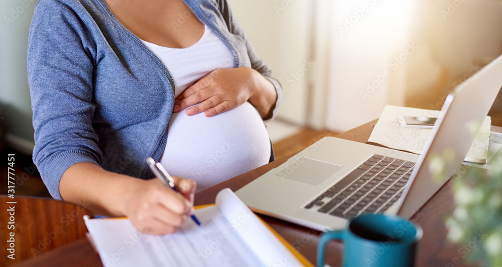 Fototapeta premium Pregnant woman writing down notes while working at home