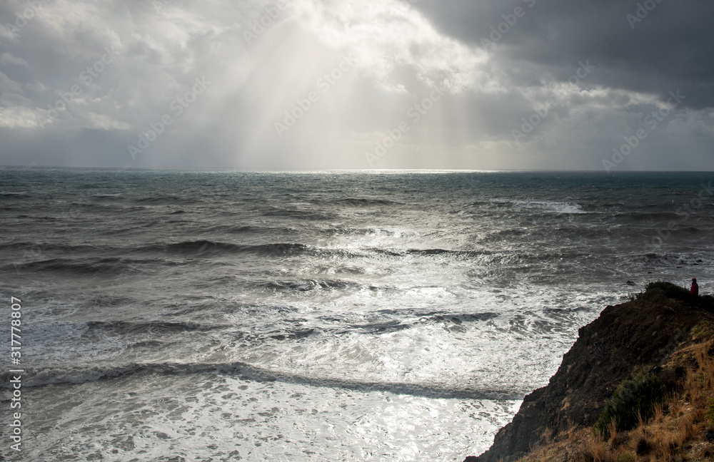 Unrecognized person standing the edge of a cliff end enjoying the dramatic stormy sea.