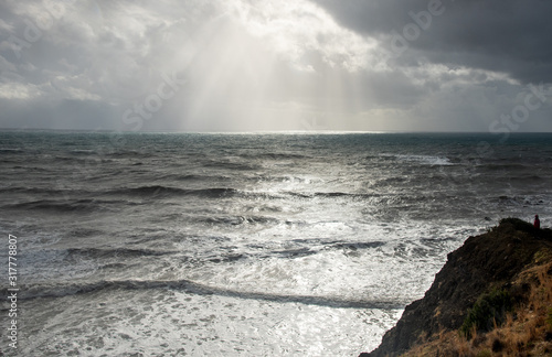 Unrecognized person standing the edge of a cliff end enjoying the dramatic stormy sea.