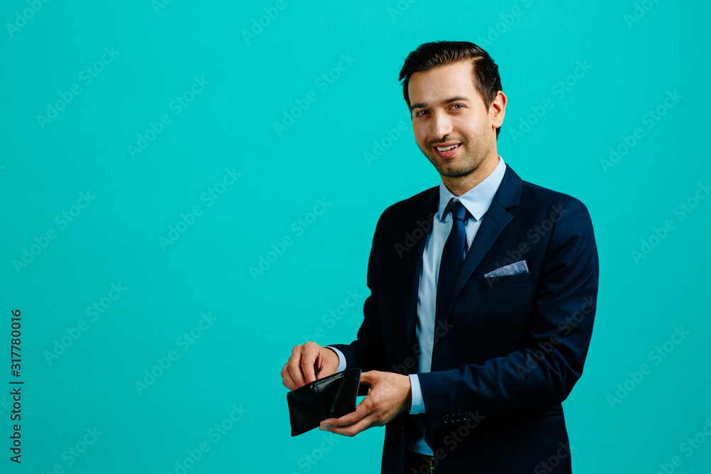 Portrait of a young entrepreneur business man pulling money from wallet,  isolated on blue studio background