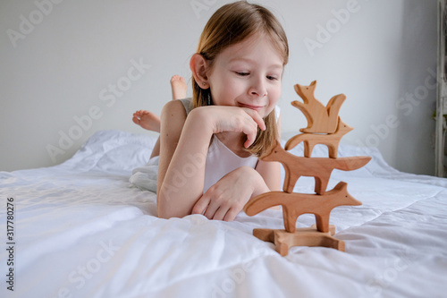 little girl of 8 years old plays with eco-friendly wooden toys in the shape of different animals