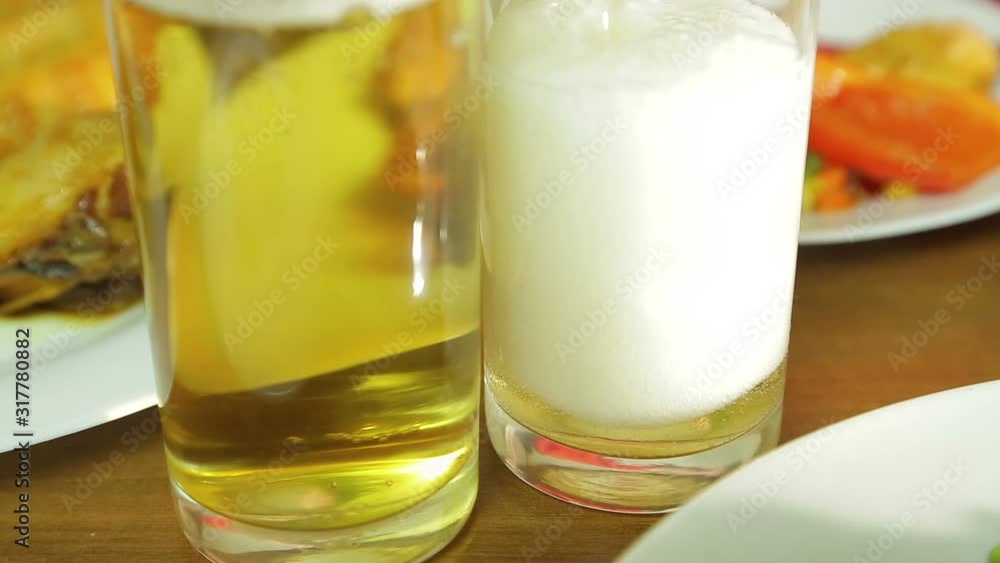 Foamy light beer from a bottle is poured into a transparent glass. Foamy light beer from a bottle is poured into a transparent glass.