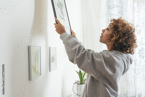 Young woman hanging up picture at home