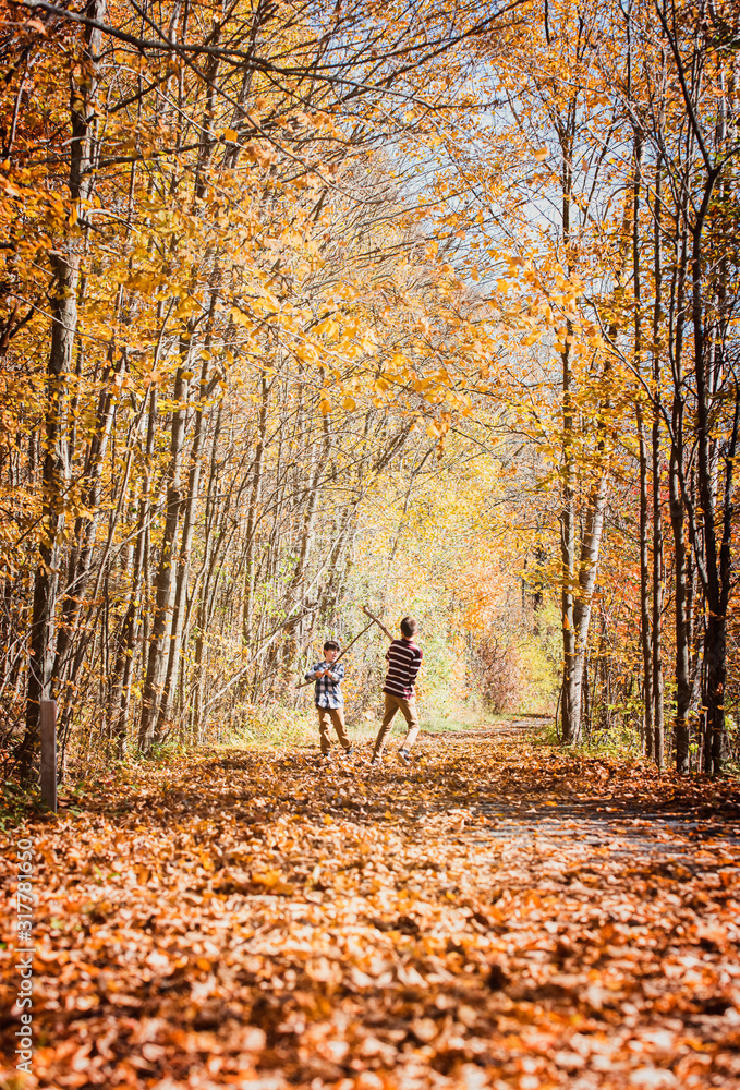 Two boys play fighting with sticks on leaf covered trail in autumn. Two boys play fighting with sticks on leaf covered trail in autumn.