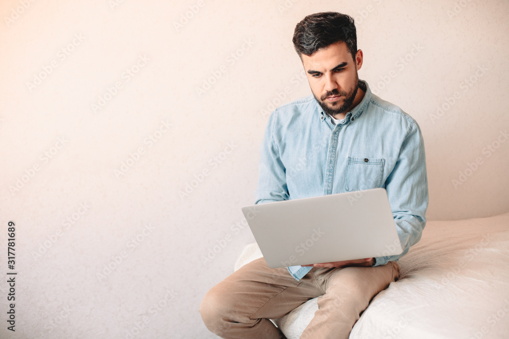 Young man using laptop computer while sitting at home against wall Young man using laptop computer while sitting at home against wall