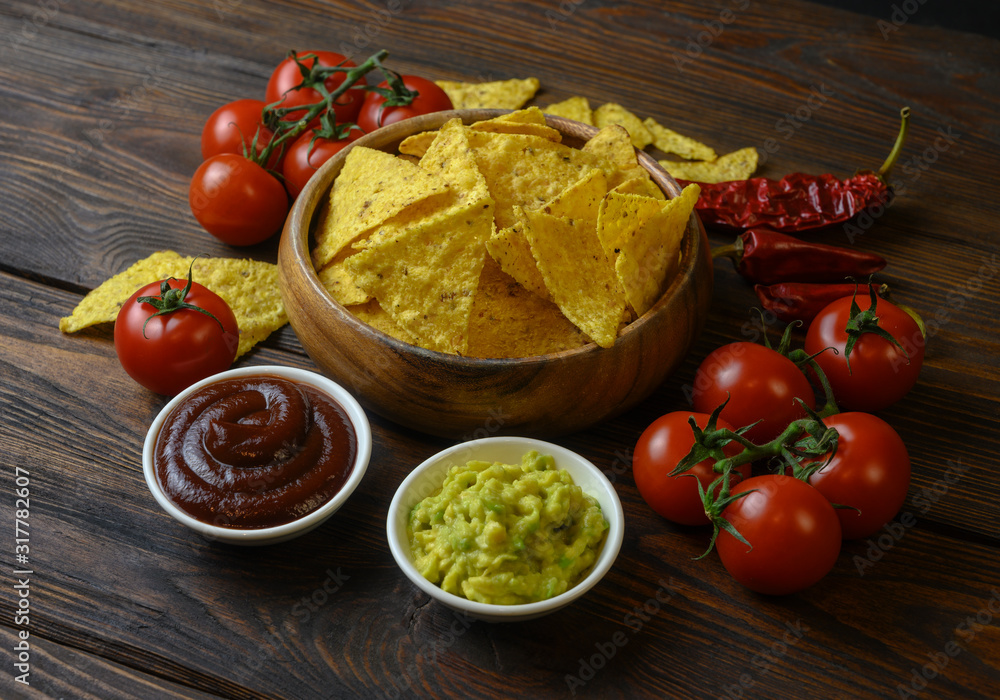 nachos in a wooden bowl and sauces on a wooden table