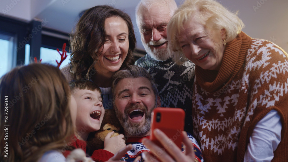 Fototapeta premium Joyful big family of three generations embrace together making a fun holiday selfie on smartphone. Full family portrait. Christmas Eve. Noel gathering.