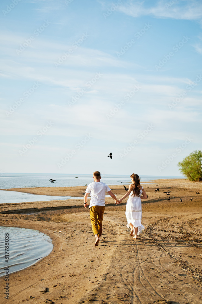 A loving couple runs barefoot along the sandy shore and hold hands, and birds fly in the distance.