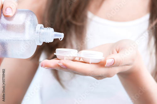 Closeup female hands are holding container for optical soft lens. Young woman is pouring contact lens solution liquid for disinfecting and clearing. Ophthalmic diseases and treatment concept. photo