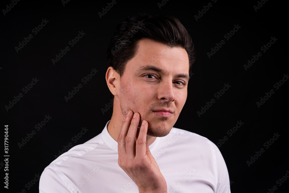 The guy in white shirt scratching his beard, uncertain. Studio with black background The guy in white shirt scratching his beard, uncertain. Studio with black background